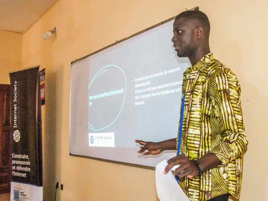 A man in a yellow shirt stands next to a projector screen
