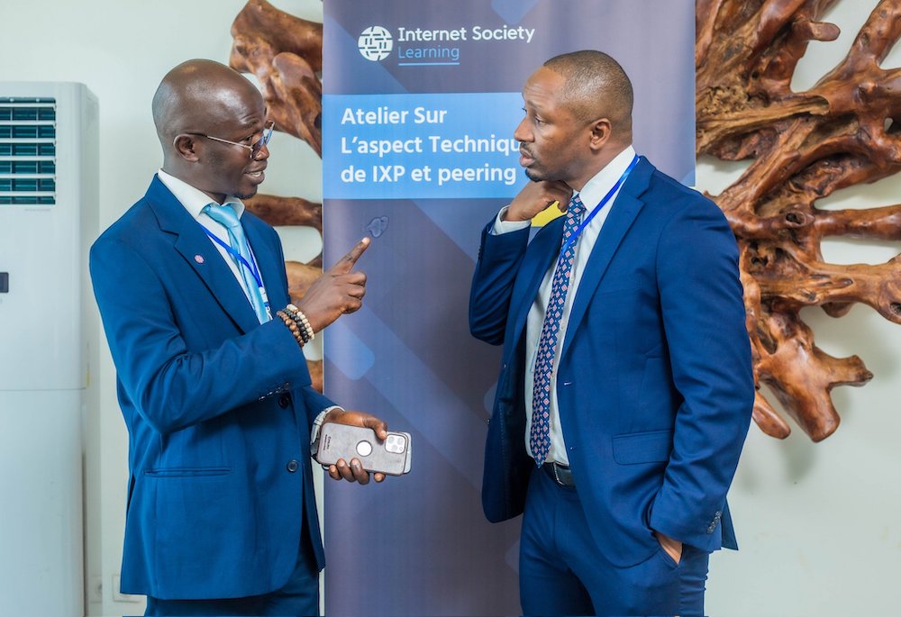 Two men in blue suits talk in front of an Internet Society Learning sign