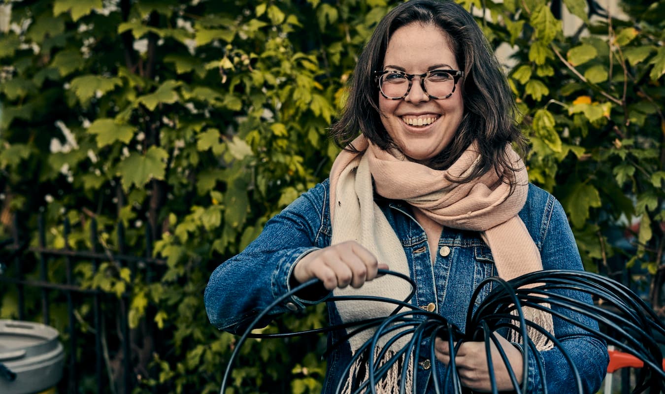 A woman wearing glasses and a scarf is holding a black wire