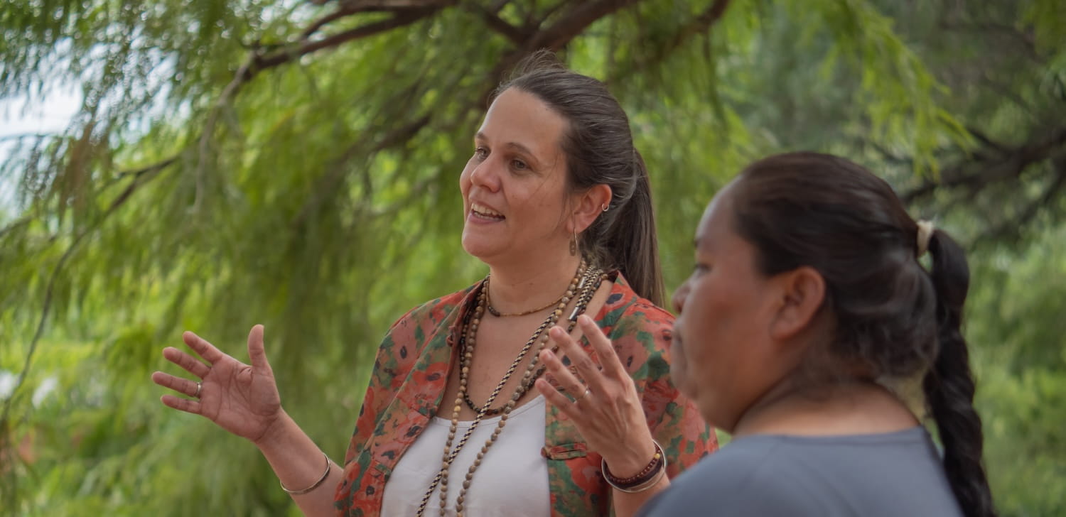 A woman engaged in conversation with a group of people, surrounded by lush green trees