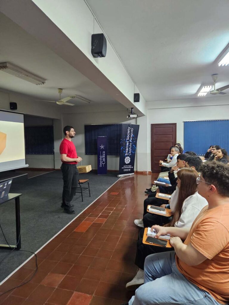 A group of seated people watch a man in a red shirt present