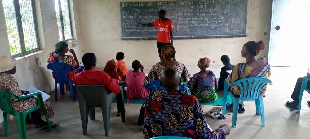 A man stands in front of a chalkboard and speaks to a seated group